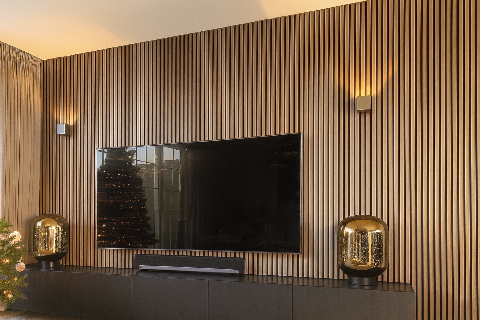 Modern living room with wall-mounted flat screen TV centered on vertical wooden slat wall, flanked by decorative gold lamps and minimalist decor