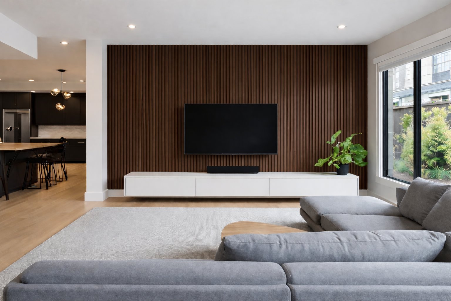 Modern living room with gray sectional sofa facing a wall-mounted TV on a brown vertical slat accent wall with white media console