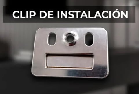 Metal installation clip with mounting holes and central screw fastener, labeled Clip de Instalación in Spanish